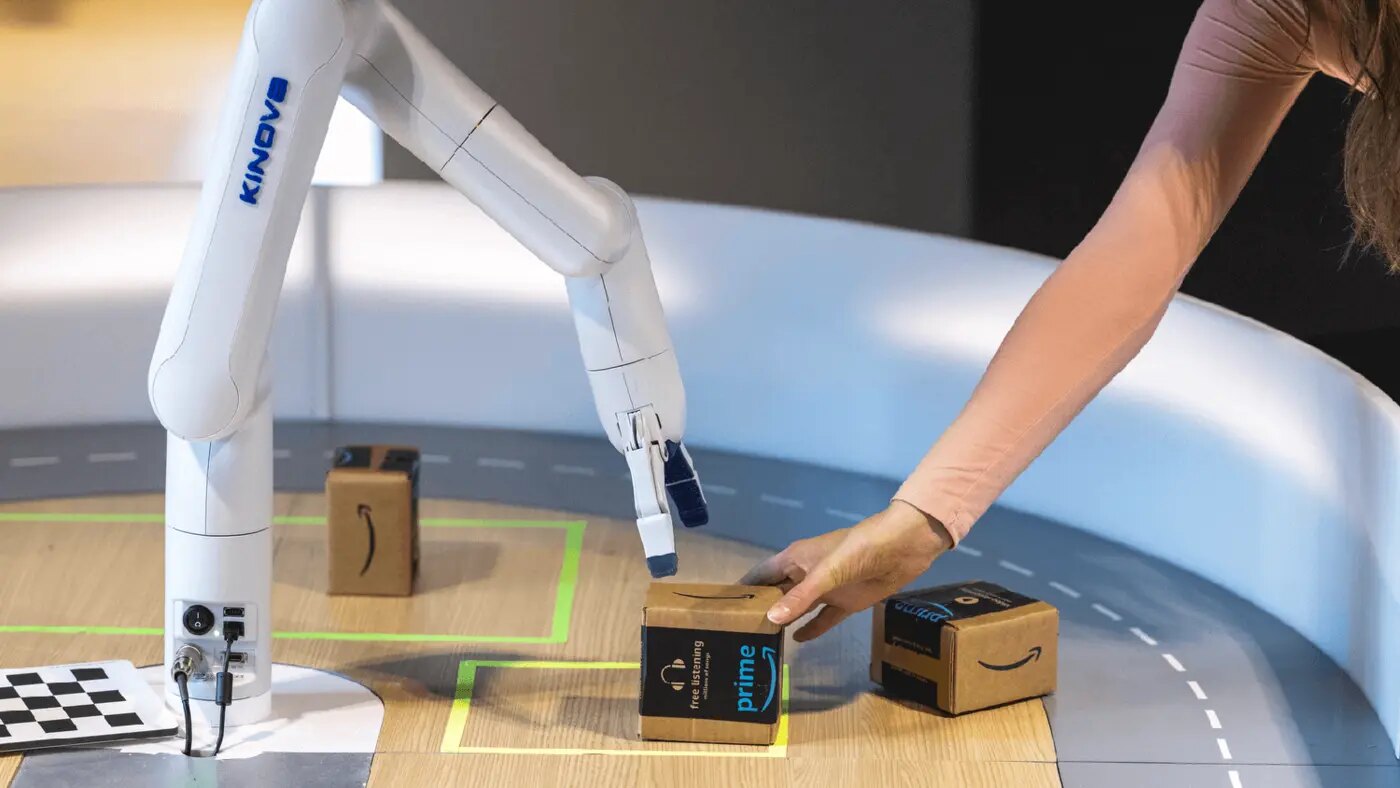 A robotic arm reaching for a cardboard box held by a human hand