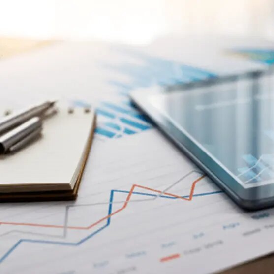 A printed economic graph beside a notebook, pens, and a tablet